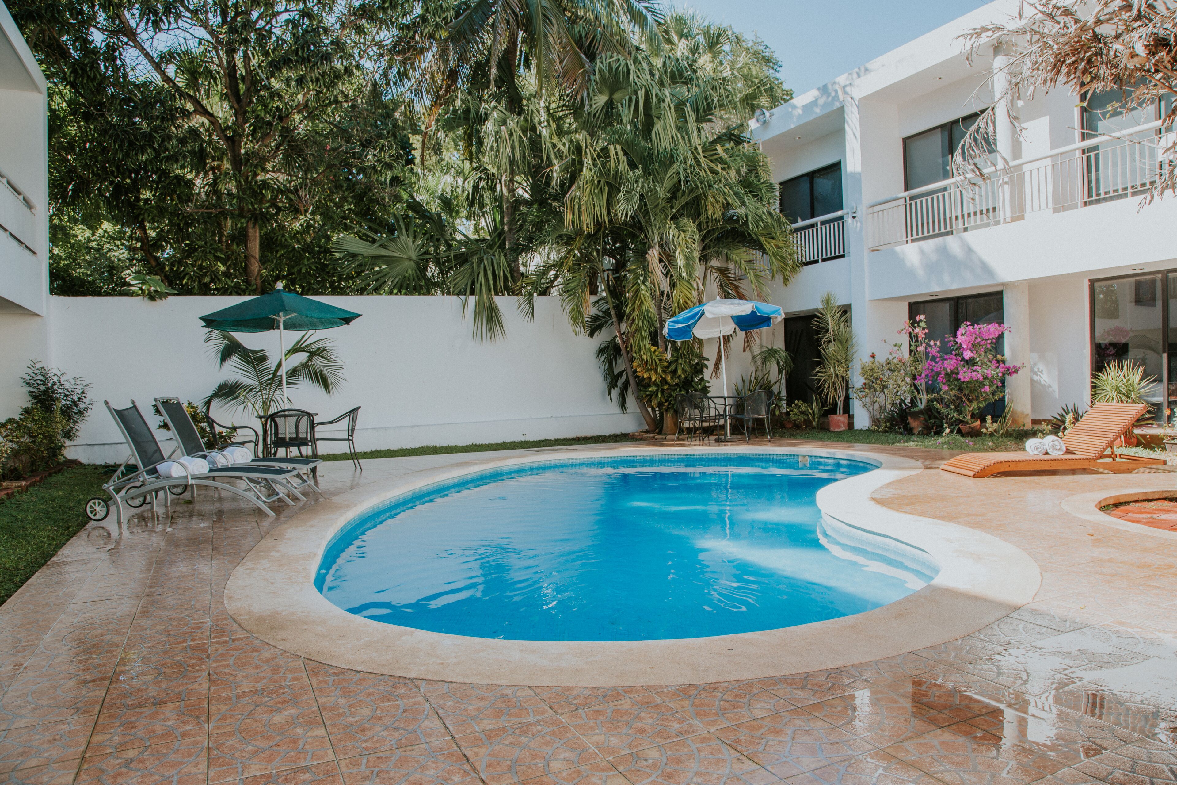 A swimming pool with lounge chairs and umbrellas, surrounded by a white building with balconies and greenery.