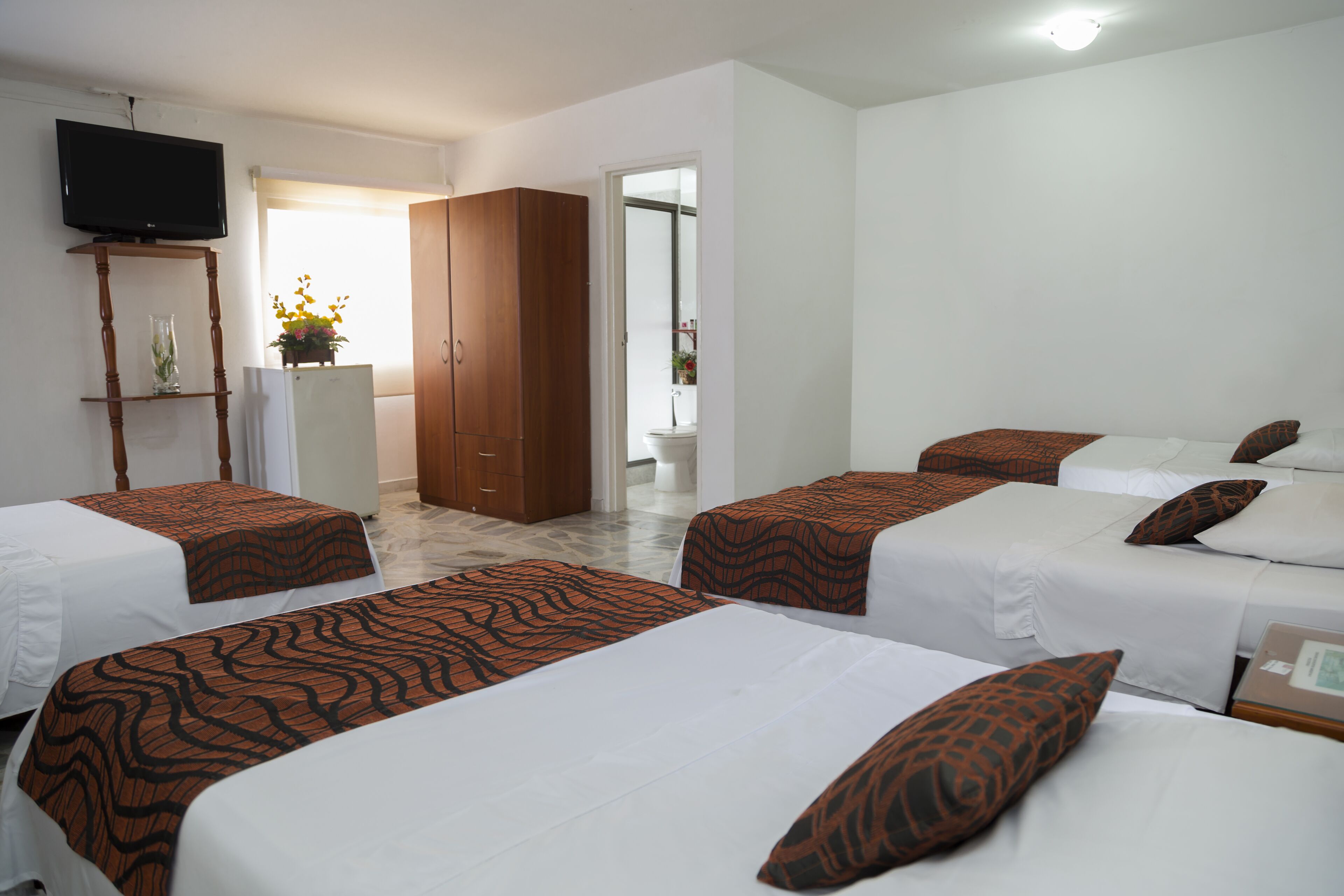 A hotel room with four beds, a TV, a wardrobe, and a bathroom visible through an open door.