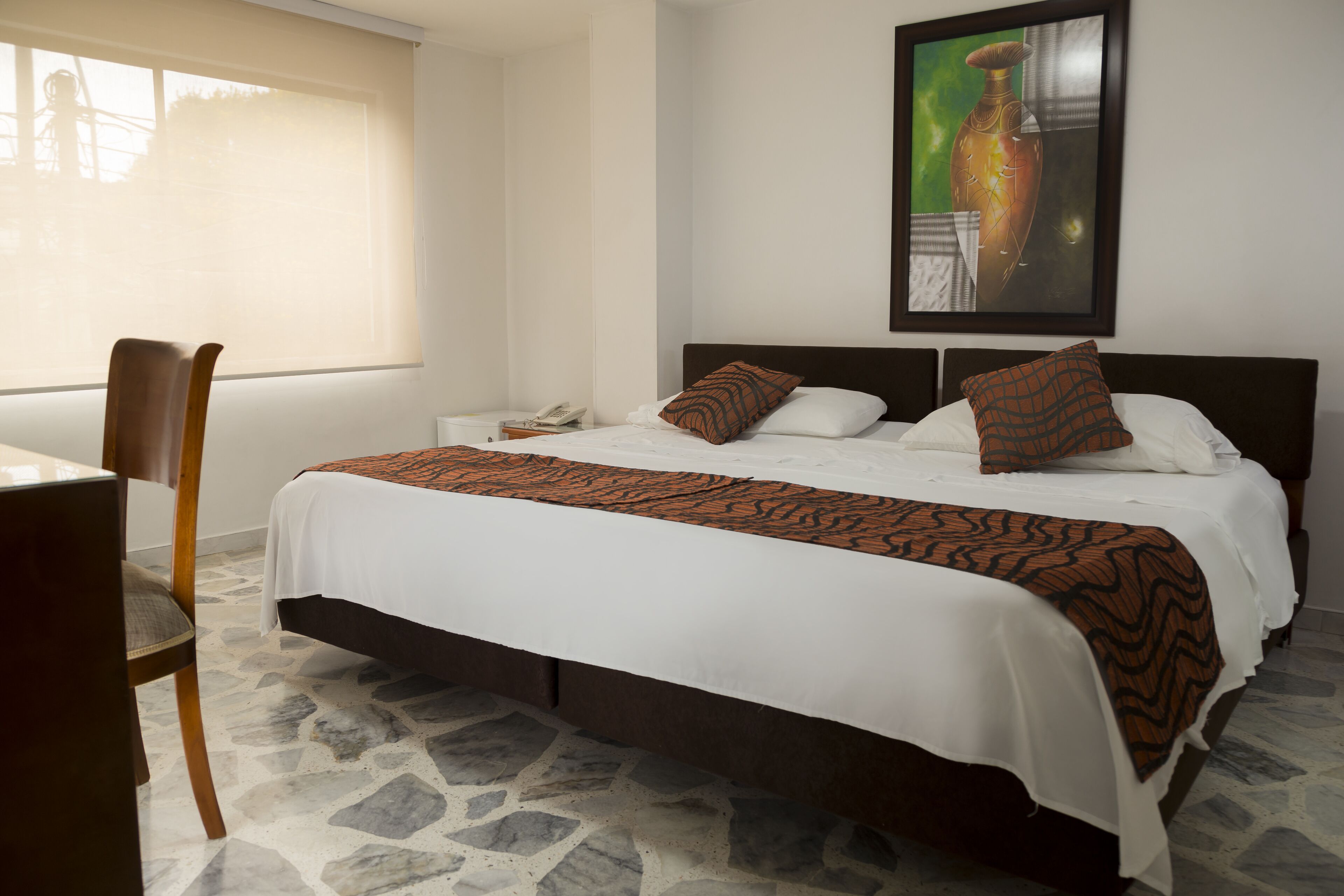 A hotel room with a bed, a chair, a nightstand, and a painting on the wall.