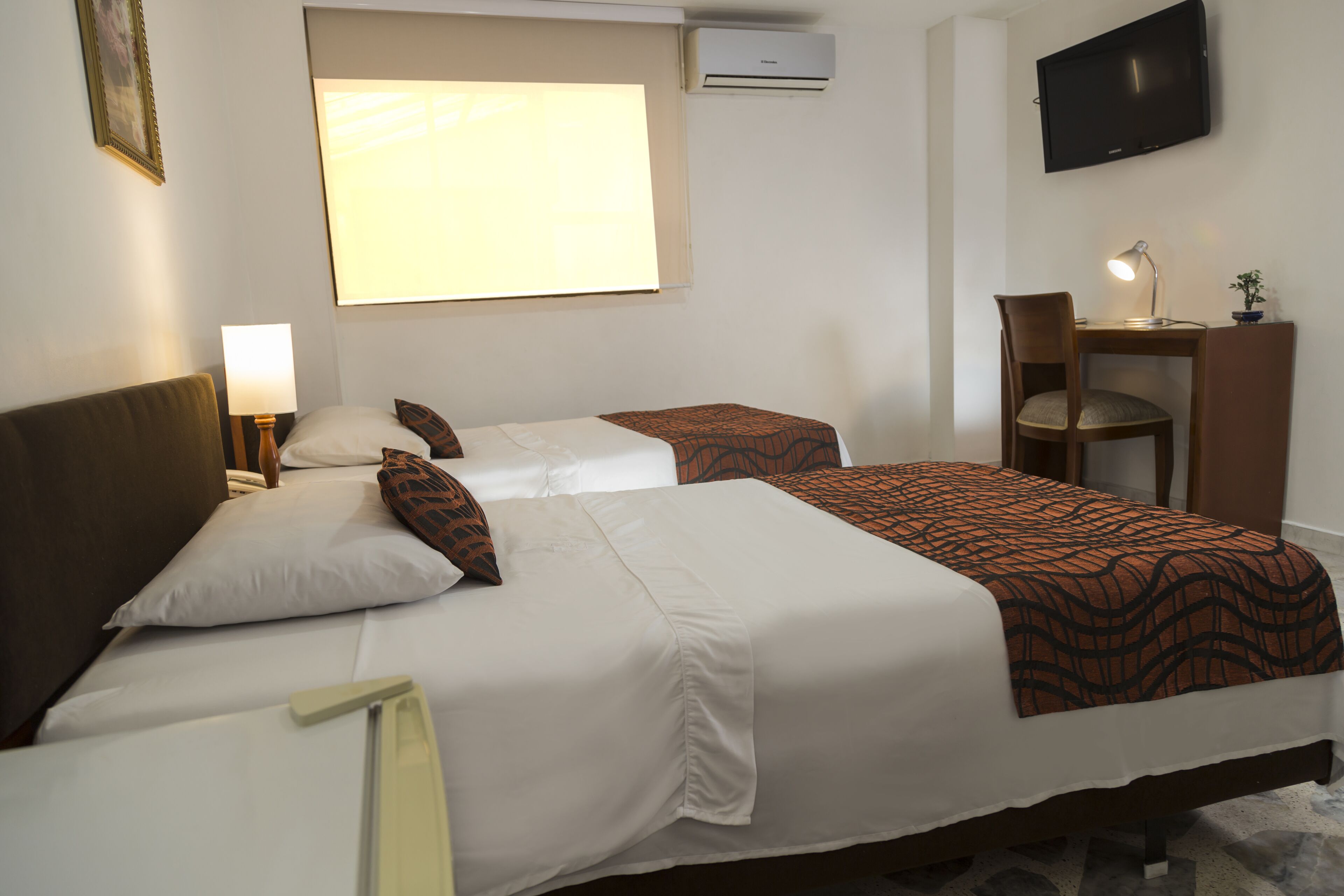 Habitación de hotel con dos camas, un escritorio, una silla, un televisor y un aire acondicionado.