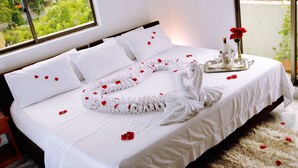 A neatly made bed with white linens, a towel arranged in a heart shape, and rose petals scattered across the bed. - Hotel Flamingo Cali (Cali)