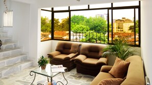 A living room with a stone floor, a glass coffee table, a brown sofa, and a view of greenery and buildings through large windows. - Hotel Flamingo Cali (Cali)