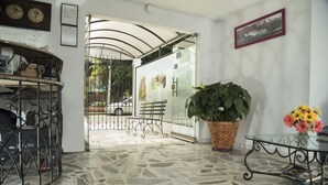 A stone-tiled lobby with a metal gate, a bench, a potted plant, and a glass table with a vase of flowers. - Hotel Flamingo Cali (Cali)