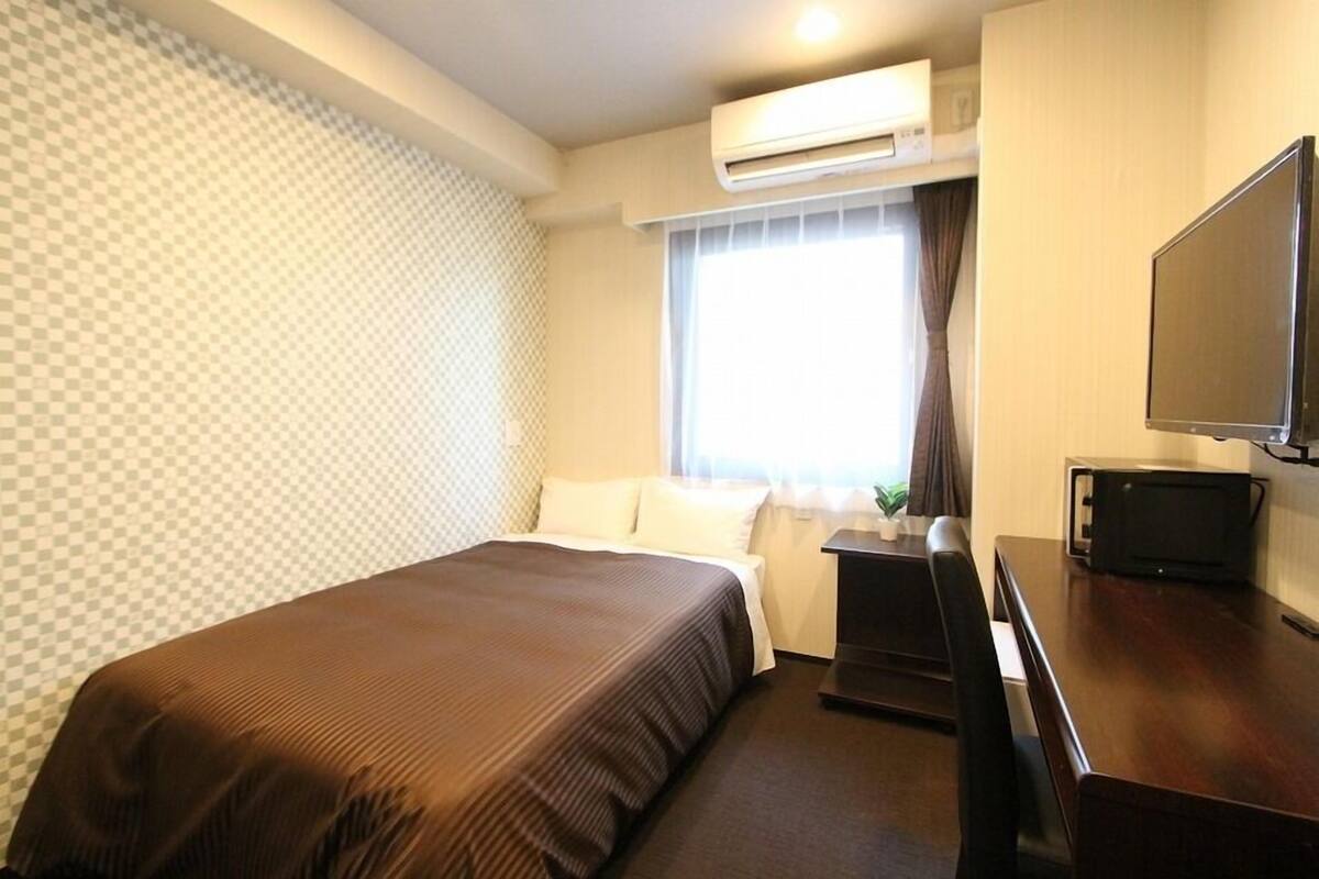 Habitación de hotel con cama, escritorio con televisor de pantalla plana, aire acondicionado y ventana con cortinas.