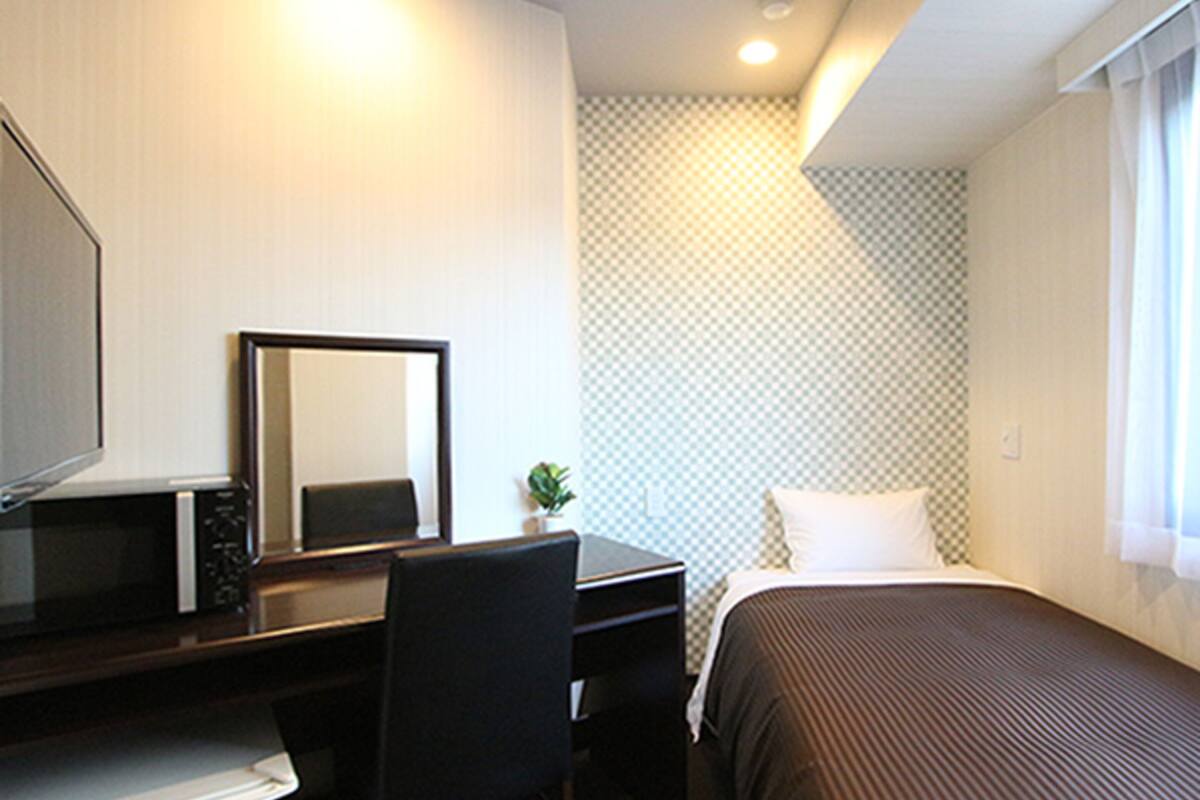 Una habitación de hotel con cama, escritorio, silla, espejo y una planta pequeña.
