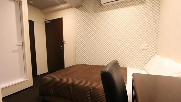 Een hotelkamer met een eenpersoonsbed, een bureau en een stoel. Er is een deur en een airconditioning in de muur.