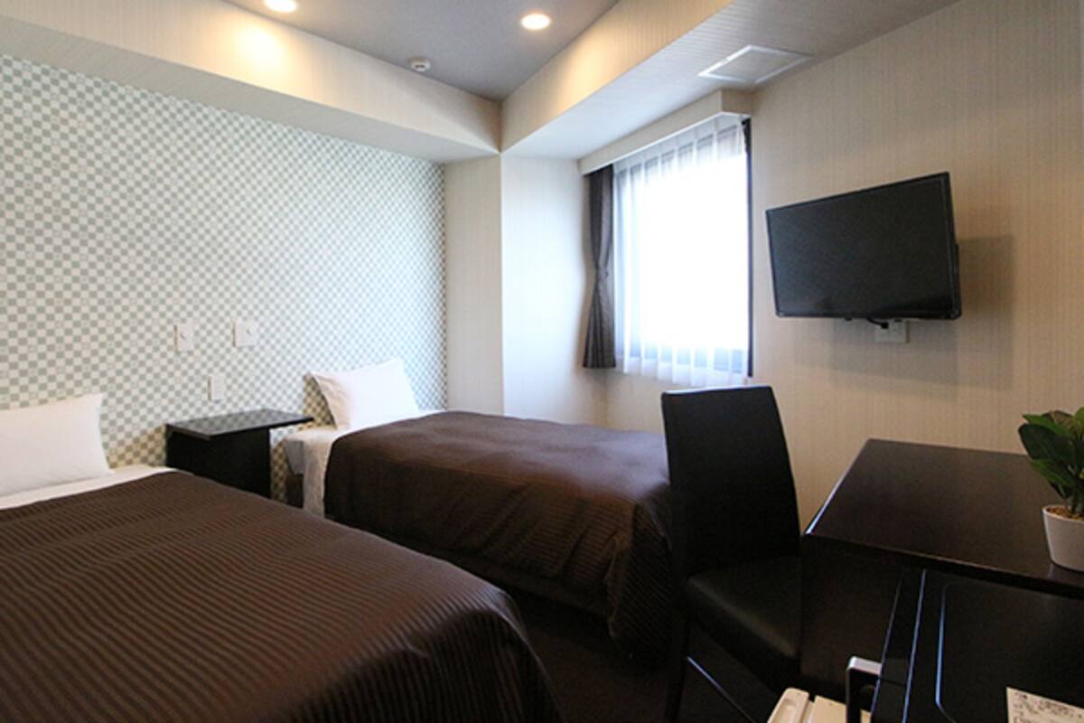 Habitación de hotel con dos camas, un escritorio, una silla, un televisor y una ventana con cortinas.
