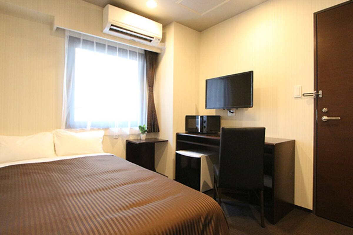 Una habitación de hotel con cama, escritorio, computadora y aire acondicionado.