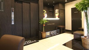 Un espace d’accueil d’hôtel comprenant un comptoir de réception, une plante, une poubelle et un coin salon.