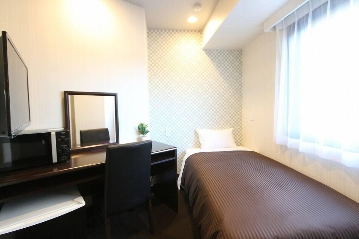 Habitación de hotel con cama, escritorio con silla, televisor y ventana con cortinas.