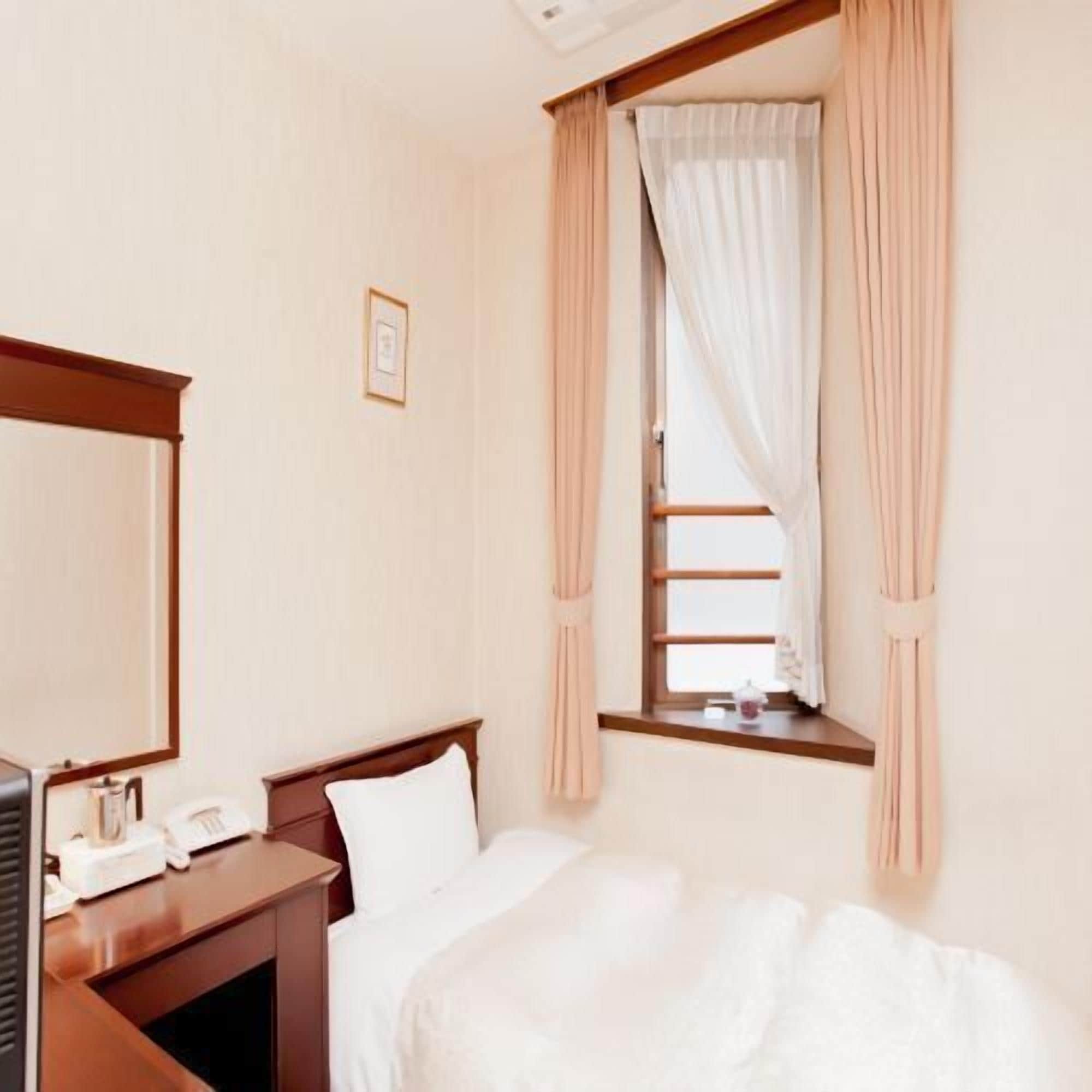 Una habitación de hotel con una cama, un escritorio con teléfono y una ventana con cortinas.