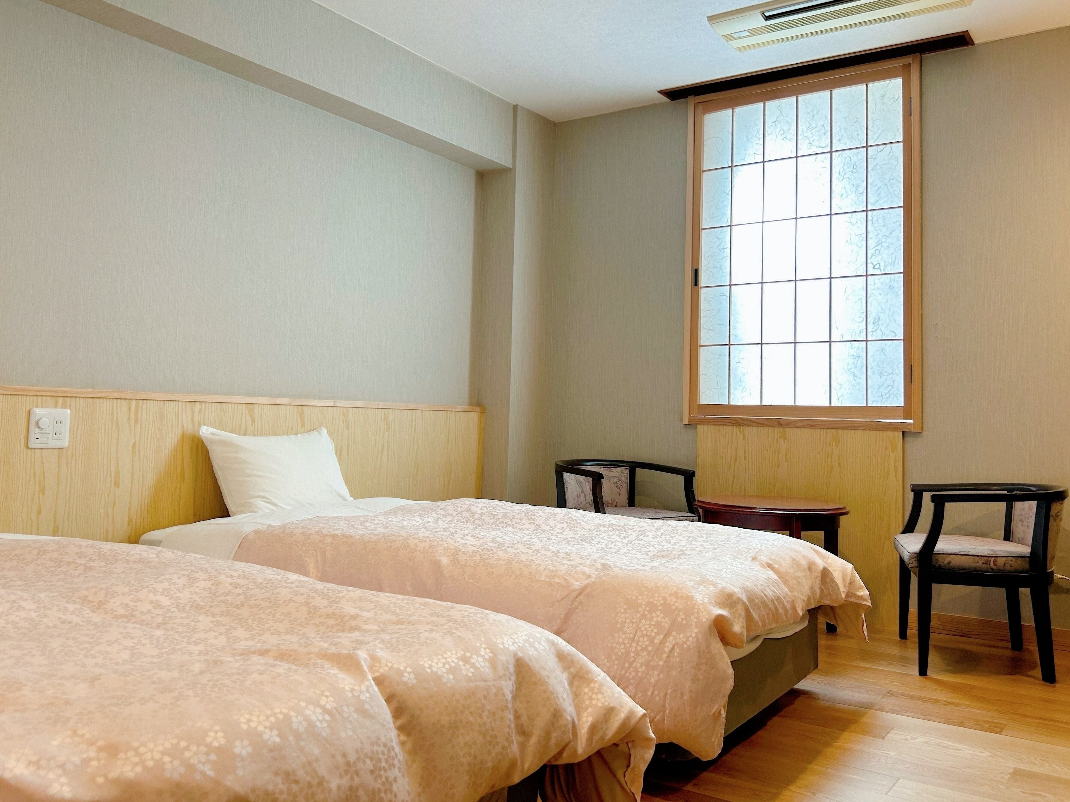 A hotel room with two beds, a window, a chair, and a small table.