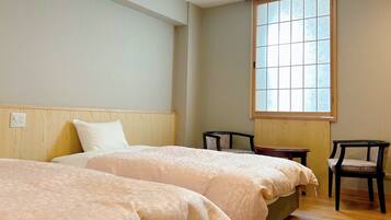 A hotel room with two beds, a window, a chair, and a small table.
