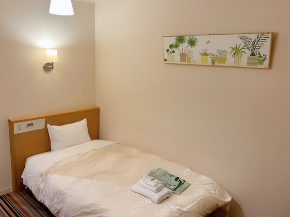 A neatly made bed with a headboard, a wall-mounted light, and a framed botanical illustration. - Hotel Hanakomichi (Nara)