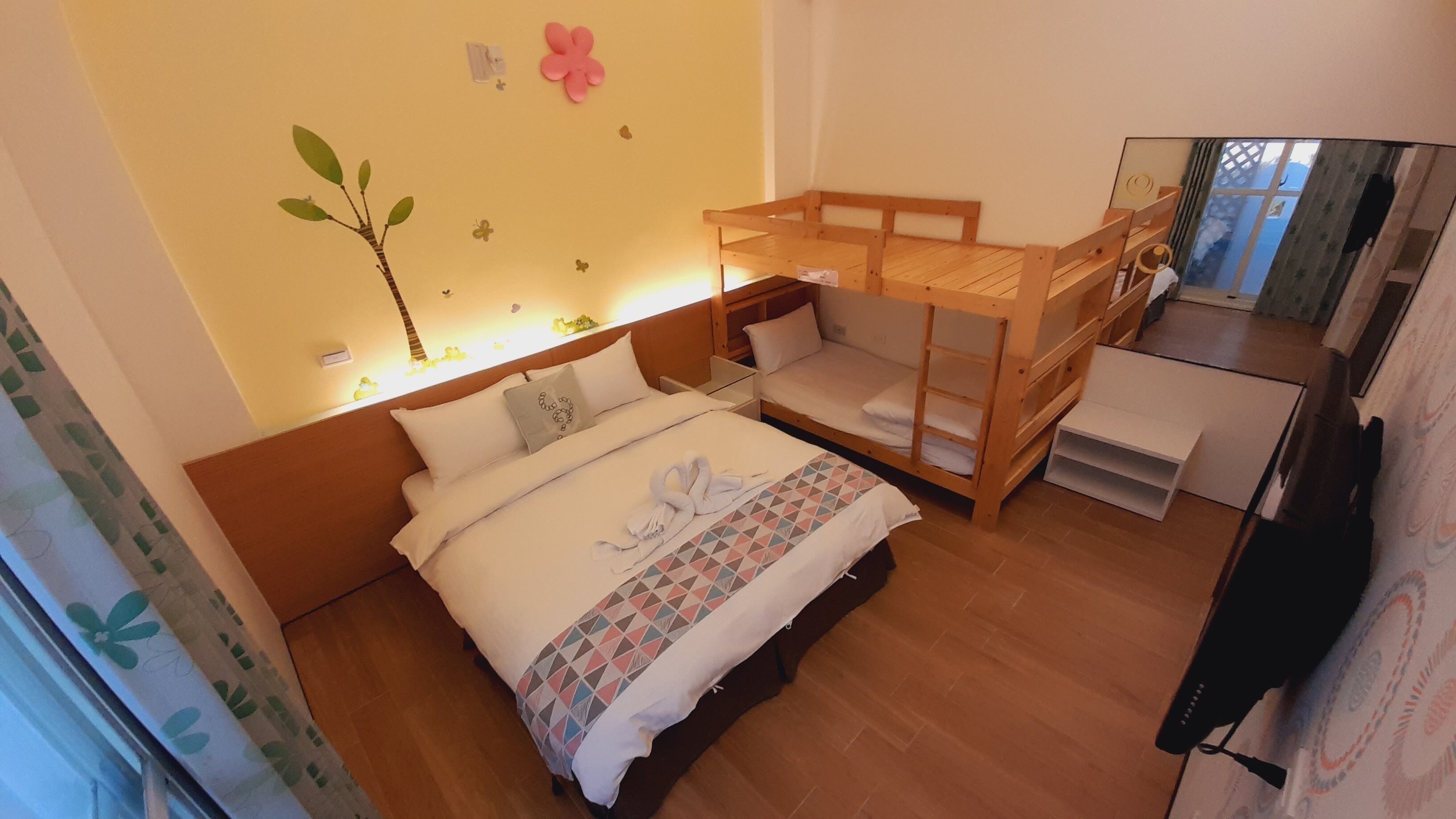 Ein Schlafzimmer mit einem hölzernen Etagenbett, einem Einzelbett mit gemustertem Bettbezug und einer Wand, die mit einem Baum und Blumen verziert ist.