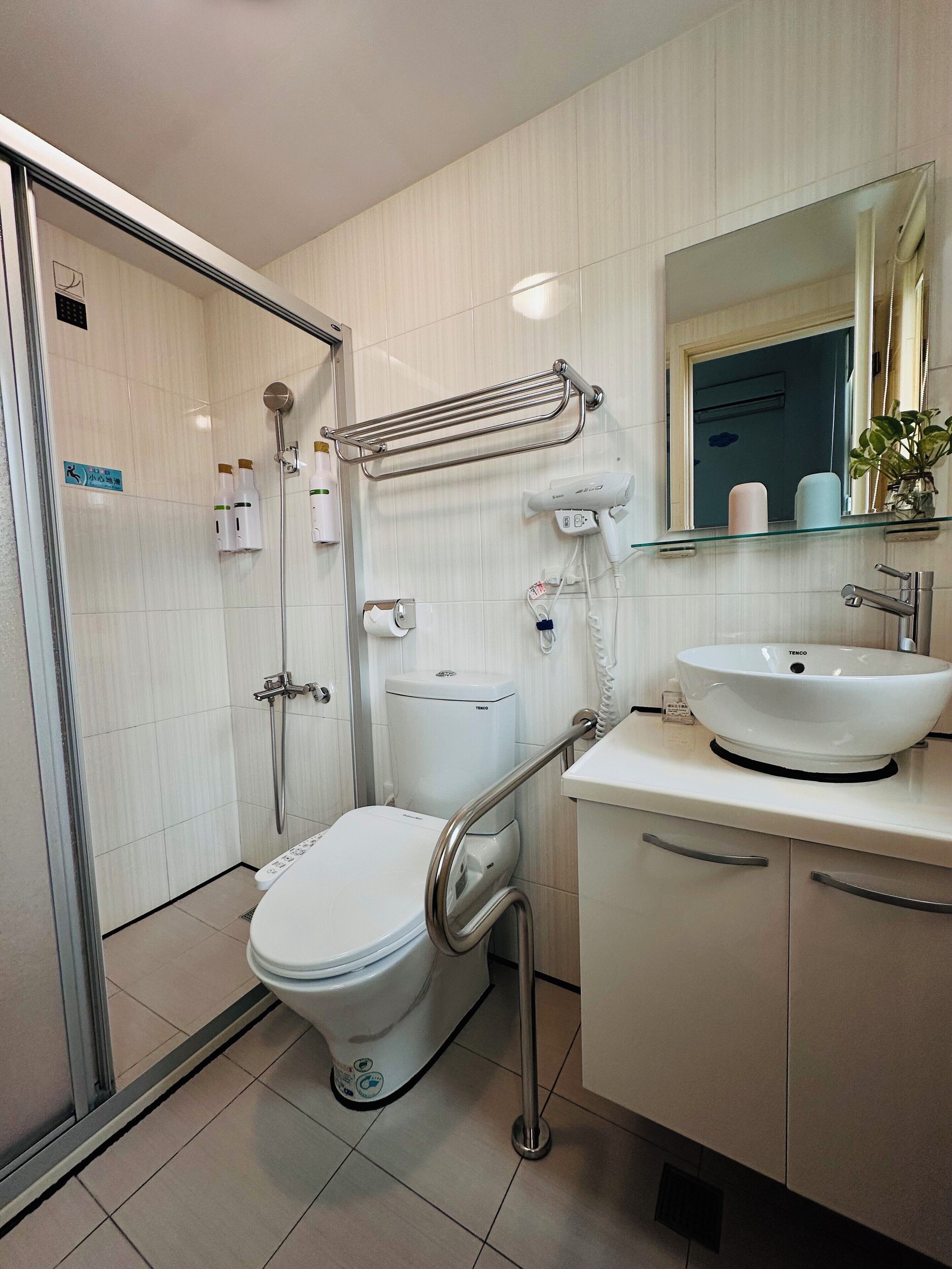 Un baño moderno con cabina de ducha de vidrio, inodoro blanco, lavamanos de vidrio y un perchero para toallas.