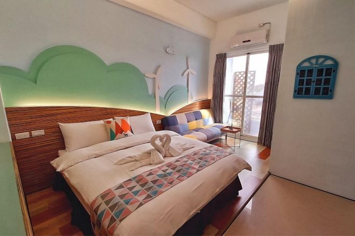 A hotel room with a bed, a sofa, a small table, and a window with curtains.
