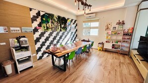 Una cocina moderna con una mesa de madera, sillas verdes, un muro con estampado blanco y negro, y una lámpara en el techo.