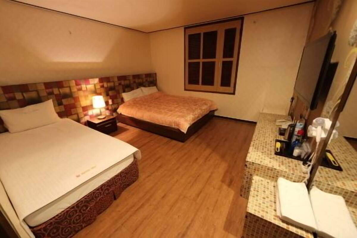 A hotel room with a bed, a nightstand with a lamp, a dresser with toiletries, and a window.