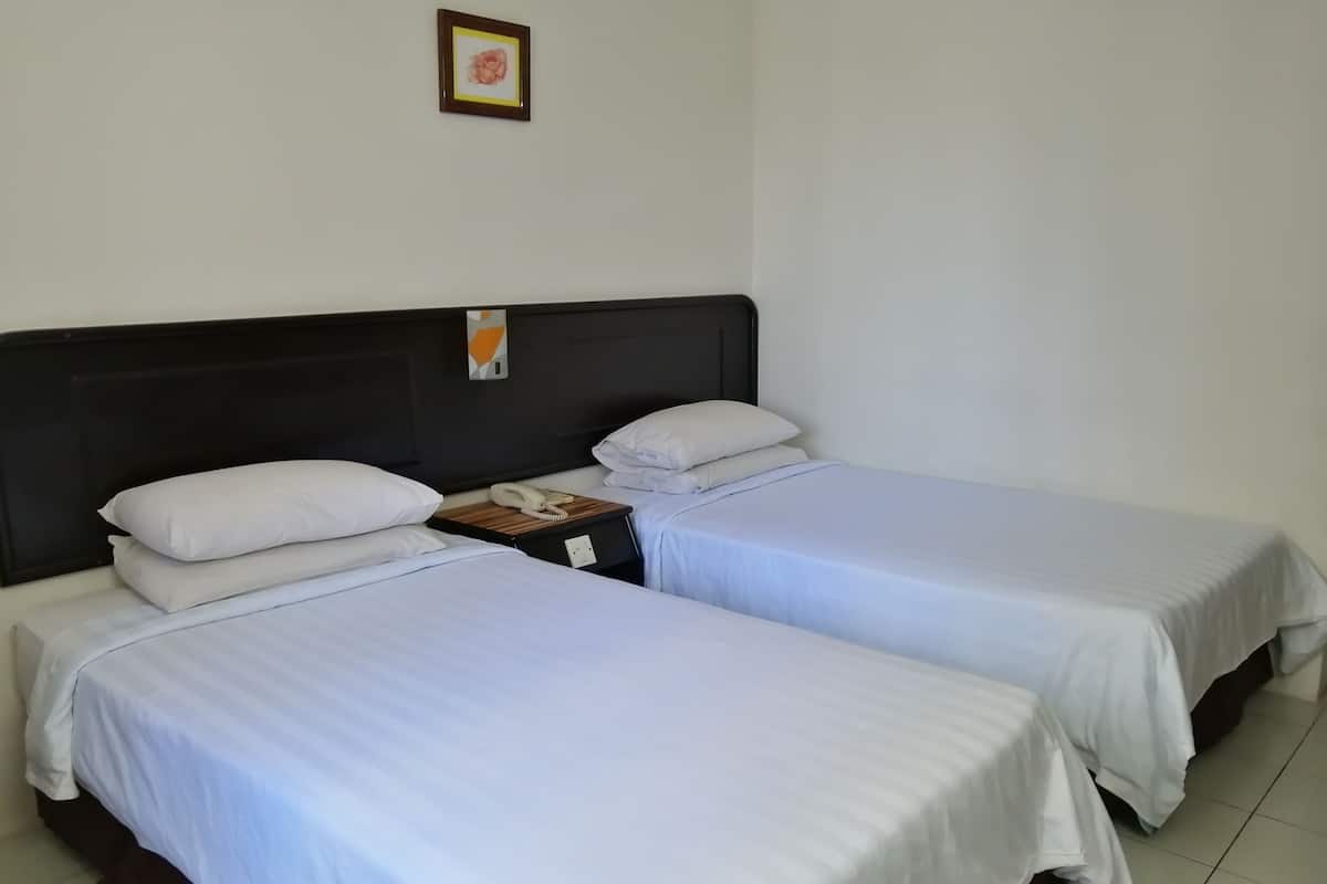 A hotel room with two single beds, white bedding, a wooden nightstand with a telephone, and a small framed picture on the wall.