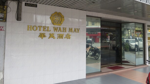 L’entrée d’un hôtel, avec une enseigne indiquant « HÔTEL WAH MAY » et un logo au-dessus.