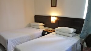 Une chambre d’hôtel avec deux lits simples, une table de chevet avec un téléphone et un luminaire fixé au mur.