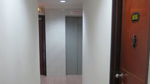 Un couloir avec un sol carrelé, une porte avec une plaque numérotée et un ascenseur à l’arrière-plan.
