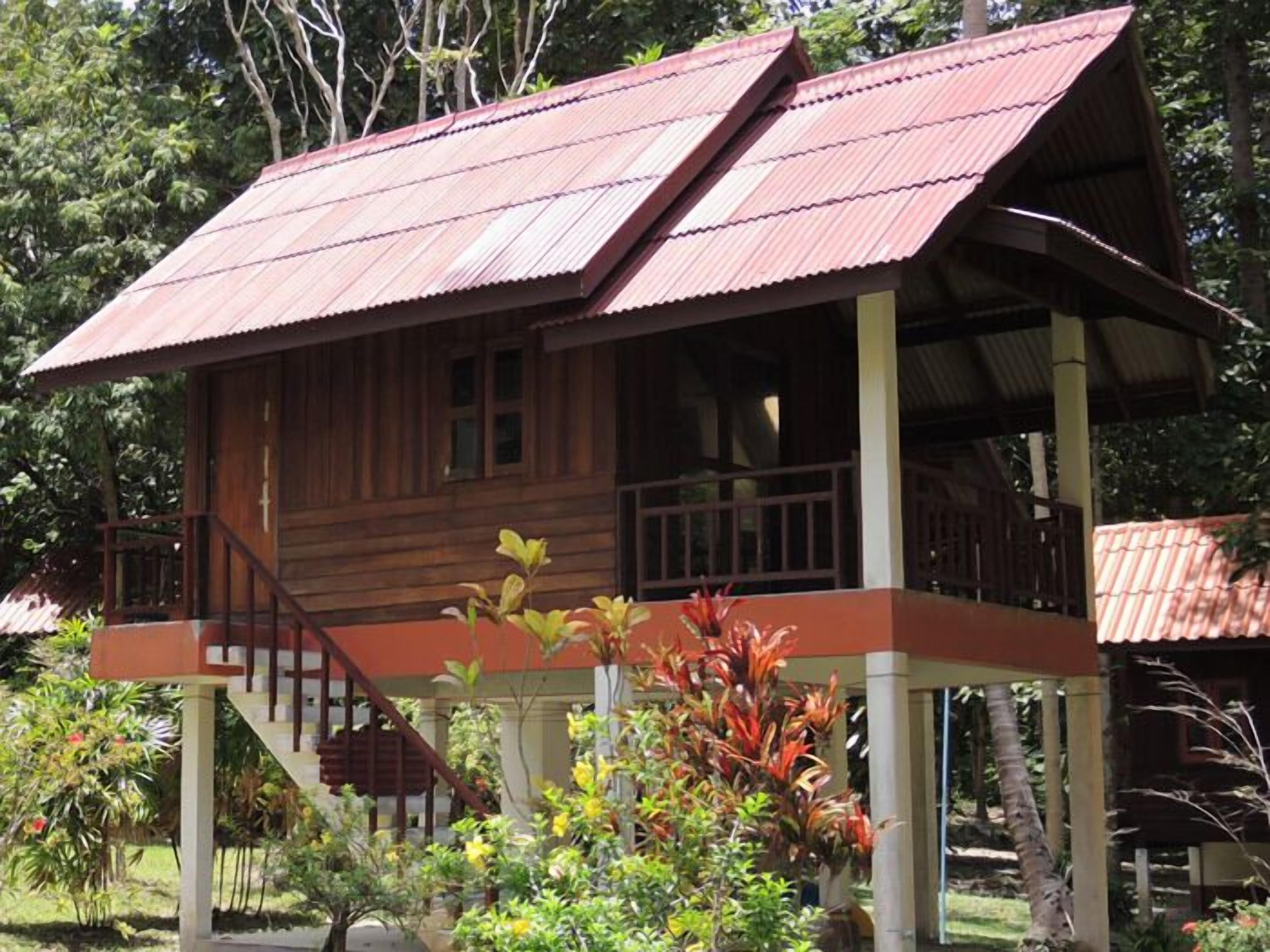 A wooden house with a red roof, a porch, and a staircase leading to the entrance.