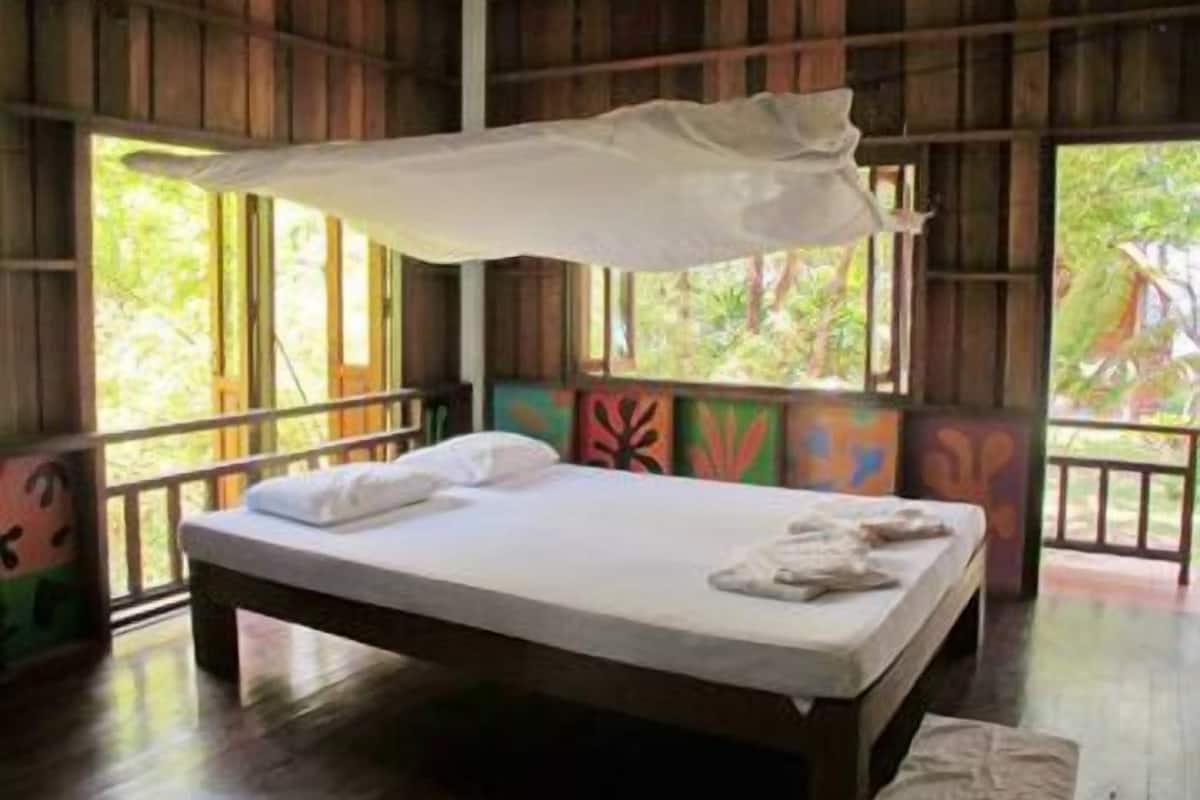A wooden room with a bed, large windows, and colorful wall art.