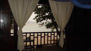 Una habitación con cama, cortinas, vista a la playa y una terraza de madera.
