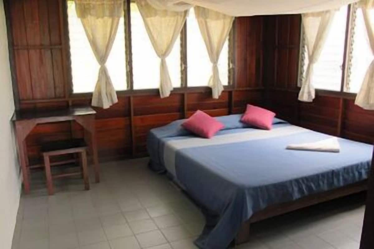 A room with a bed, two pillows, a small table, and curtains.