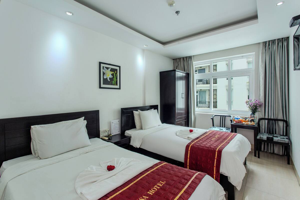 A hotel room with two beds, a desk, a chair, and a window with curtains.