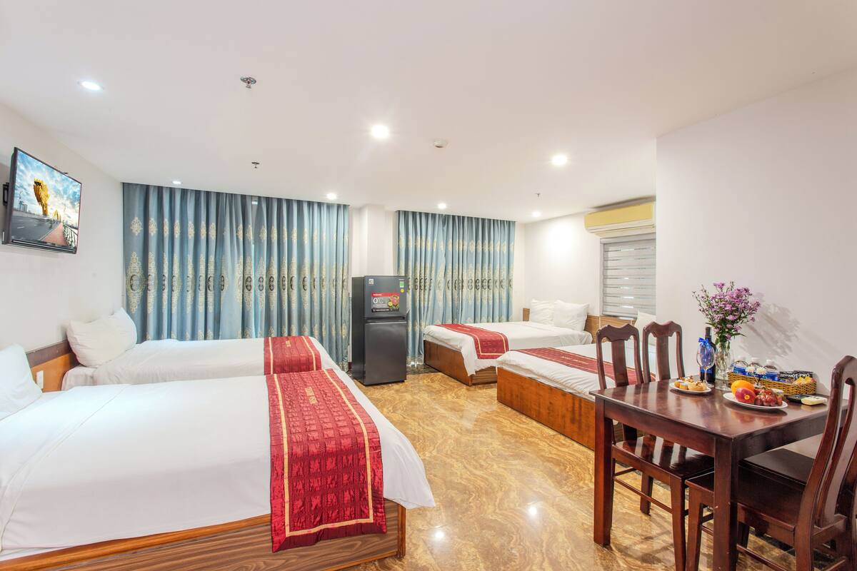 A hotel room with two beds, a dining table, and a refrigerator.