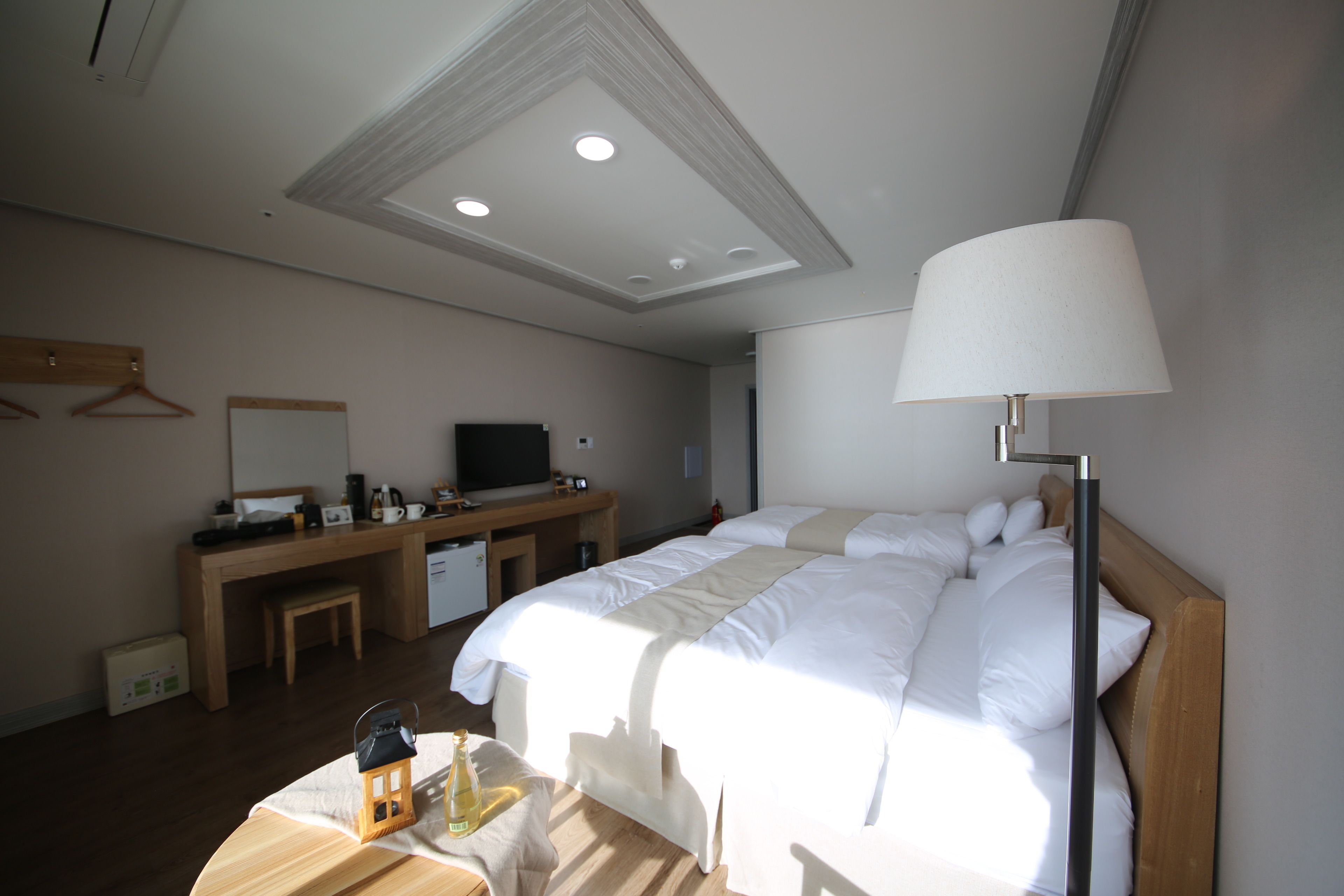 Une chambre d’hôtel avec un grand lit, un bureau avec une télévision, une petite table avec une bouteille et une lampe.