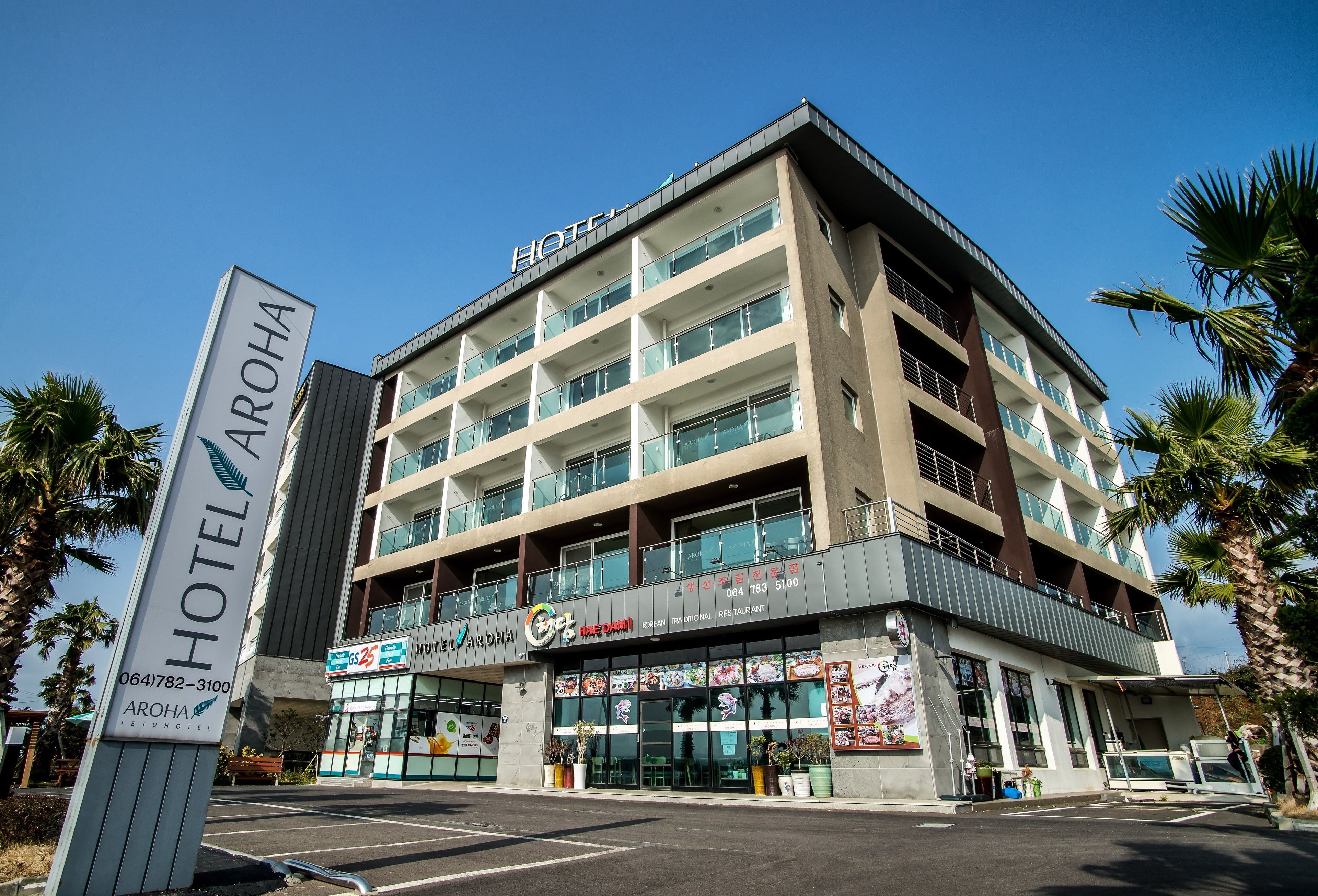 Un hotel de varios pisos con un diseño moderno, que presenta un letrero llamativo del hotel AROHA.