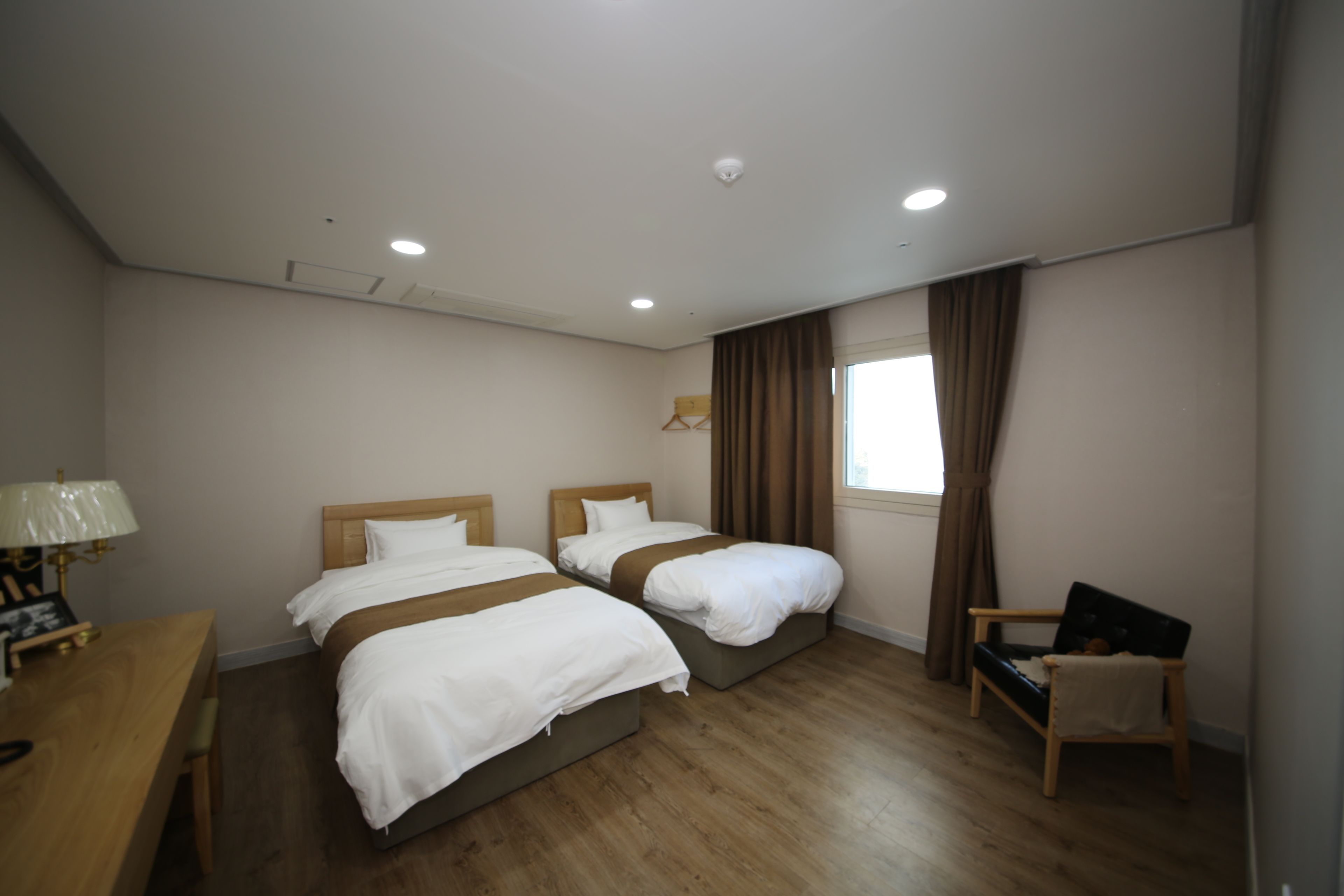 Una habitación de hotel con dos camas, un escritorio, una silla y un ventanal con cortinas.