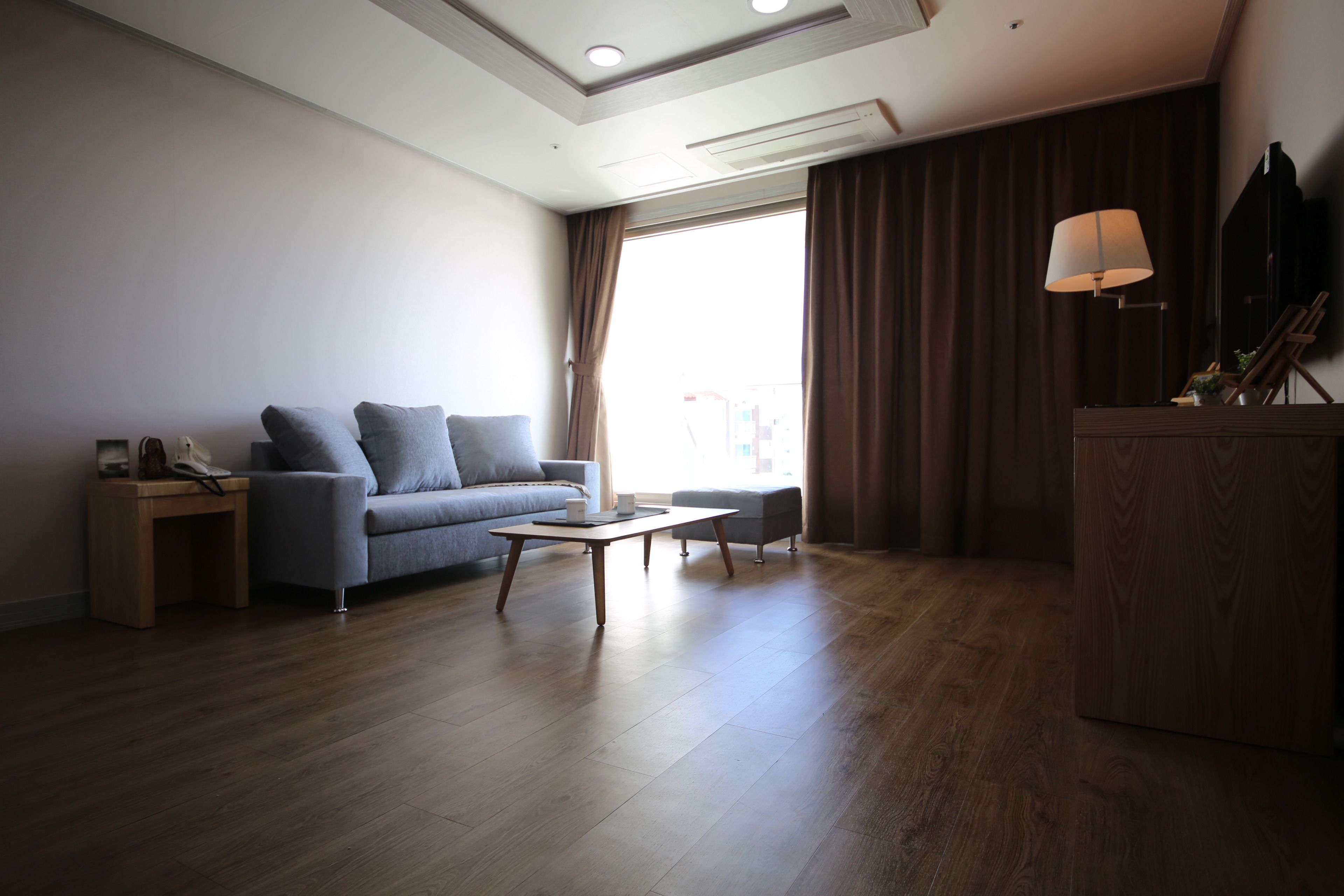 Un salon moderne avec un canapé, une table basse, un meuble en bois et une grande fenêtre avec des rideaux.