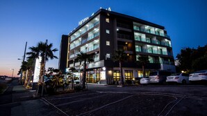 Un hotel de varios pisos con diseño moderno, que cuenta con balcones en cada planta y un área de estacionamiento al frente.