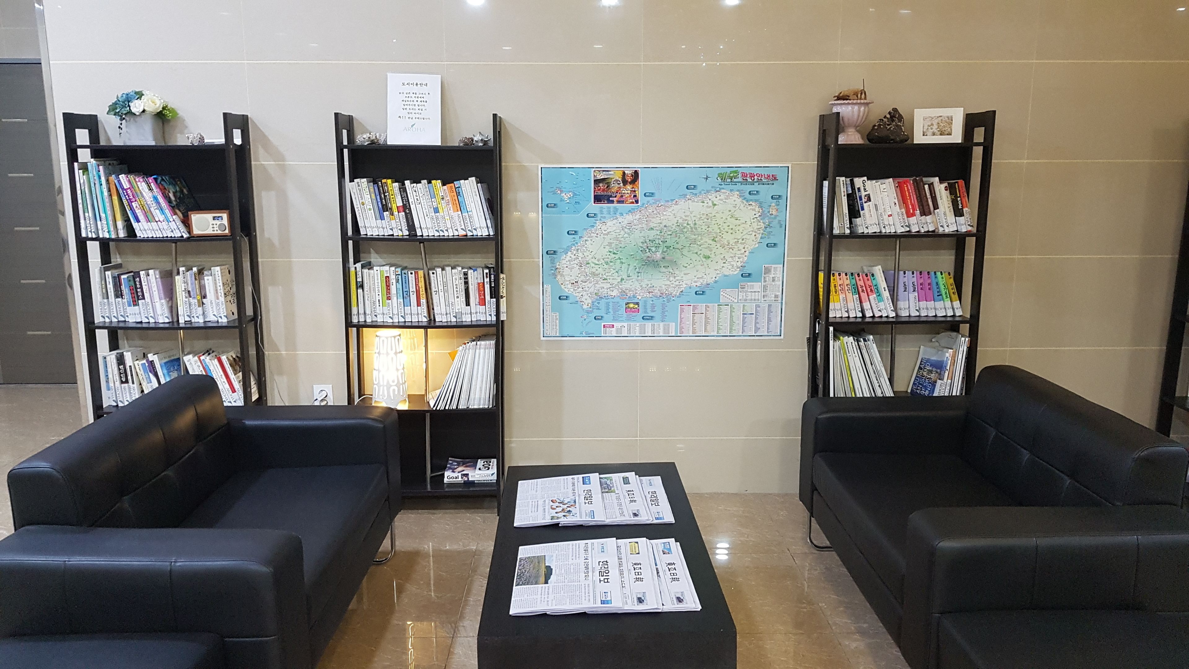 A library with black leather sofas, a coffee table with newspapers, and bookshelves filled with books and magazines.