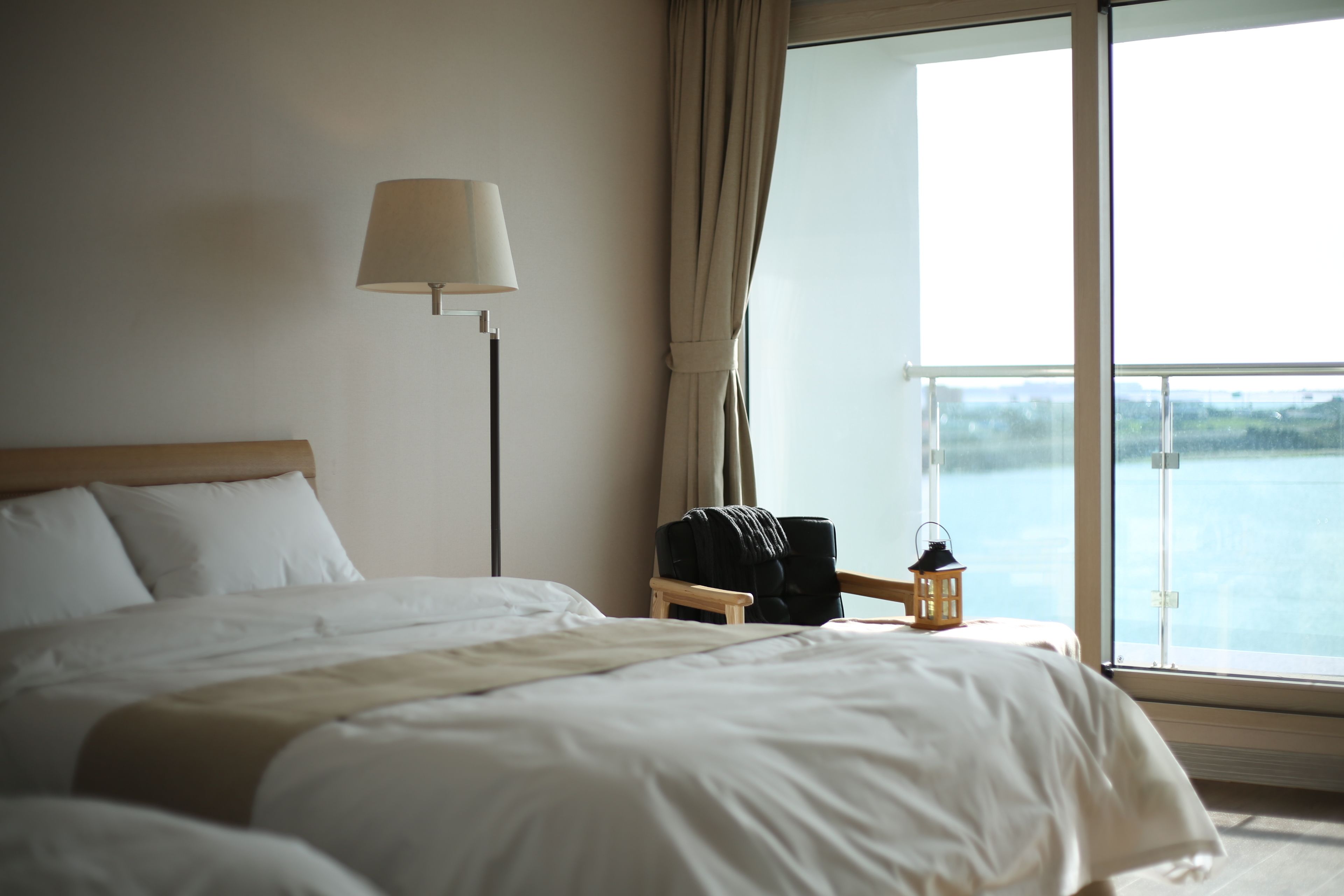 A hotel room with a large bed, a nightstand with a lamp, and a view of the water through the window.