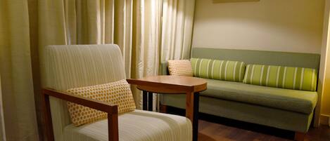 A room with a wooden floor, a green sofa, a striped armchair, and a small wooden table.