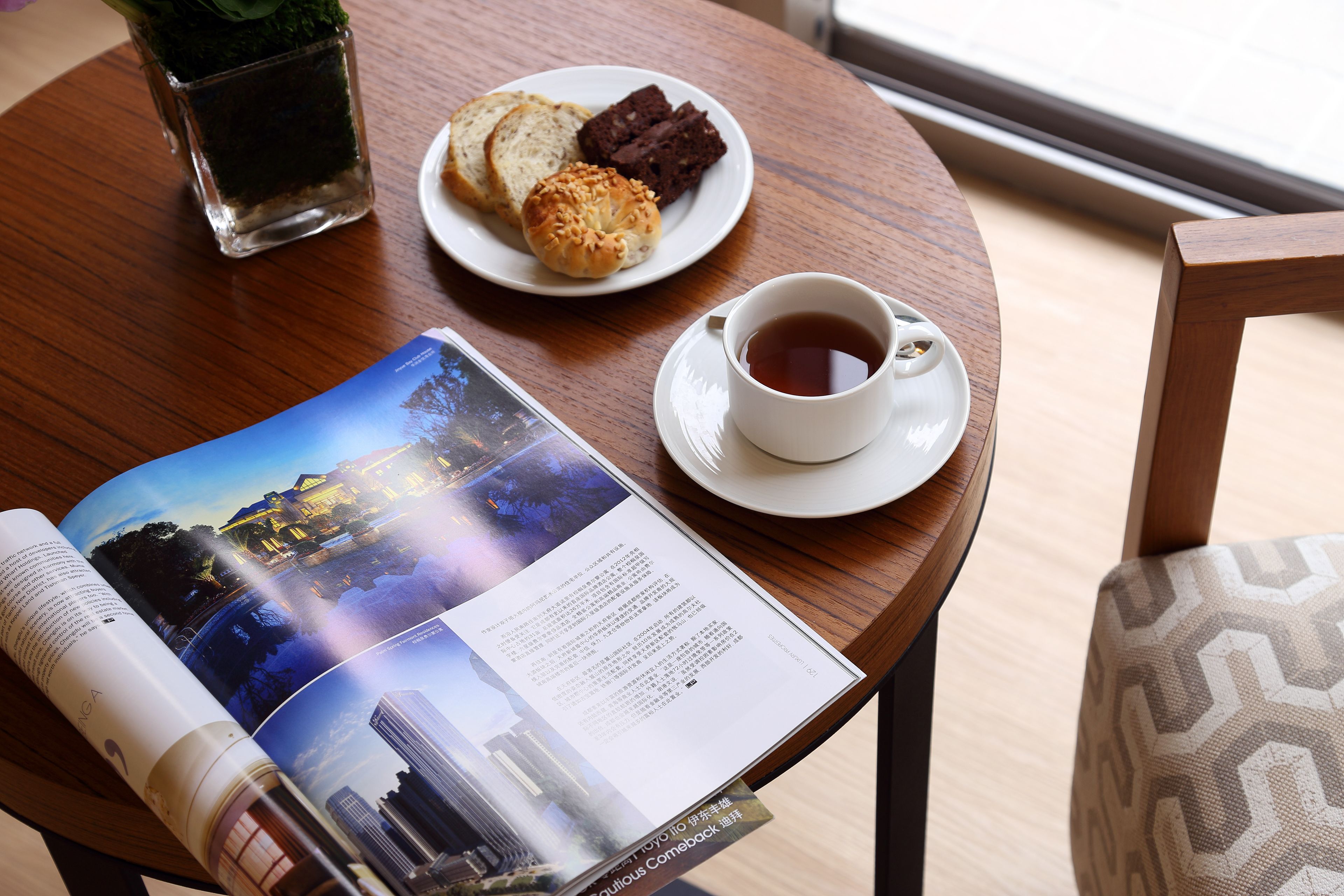 A table with a plate of pastries, a cup of tea, and a magazine.