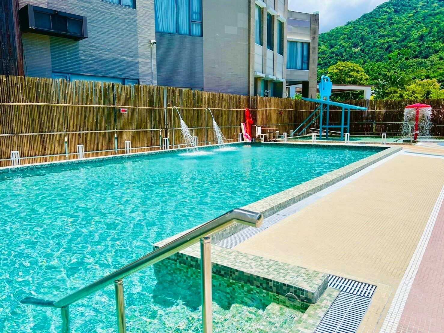 Piscina com cerca de madeira, escorrega e vista para uma montanha.