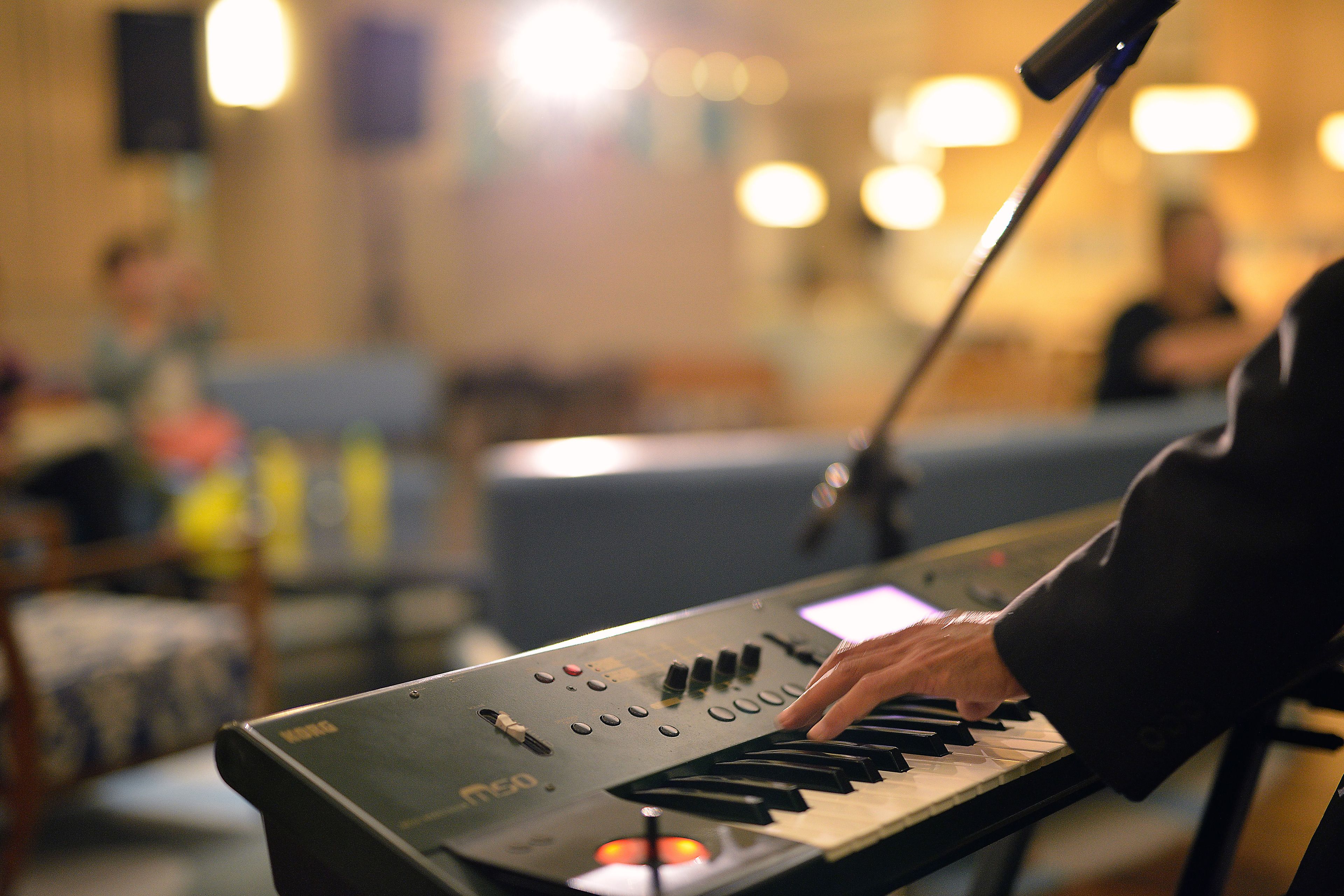 A person playing a keyboard in a room with a microphone stand and a blurred background.