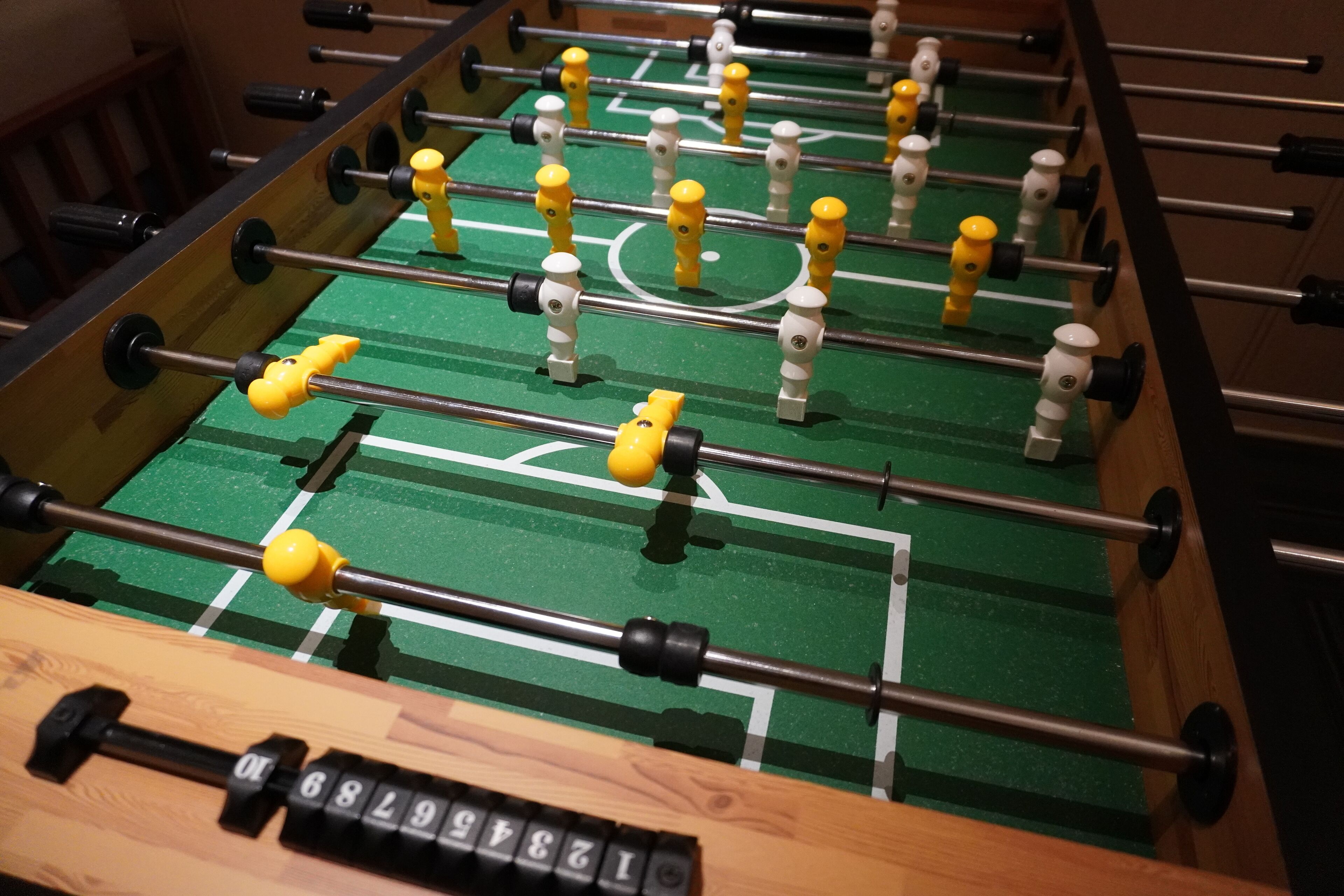Une table de baby-foot avec un tapis de jeu vert et plusieurs tiges sur lesquelles sont fixées des figurines jaunes et blanches.