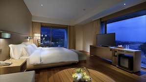A modern hotel room with a large bed, a flat-screen TV, a desk with a phone, and a view of the city at dusk. - Chihpen Century Hotel (Taimali)