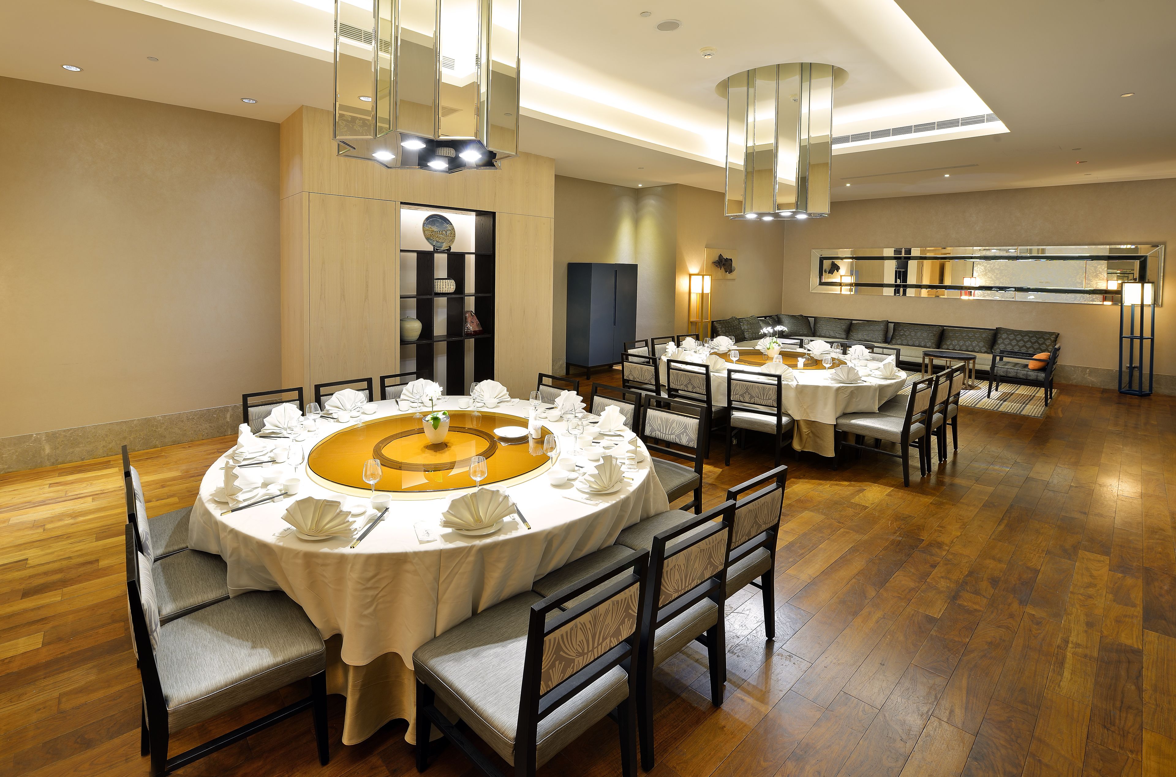 Un comedor con mesas redondas dispuestas para una comida, piso de madera y luminarias modernas.