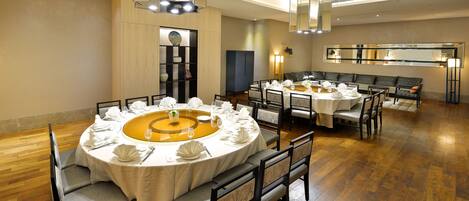 Un comedor con mesas redondas dispuestas para una comida, piso de madera y luminarias modernas.