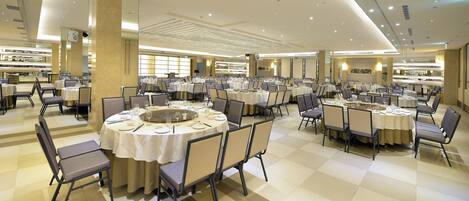 A spacious banquet hall with multiple round tables, each set with chairs and tableware, and a central decorative element.