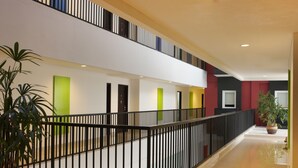 A modern hotel interior with a spacious corridor, black railings, and potted plants. - Amaris Hotel Malang (Malang)